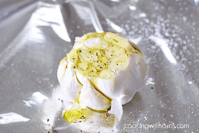 A head of garlic on foil drizzled with olive oil and sprinkled with salt and pepper.