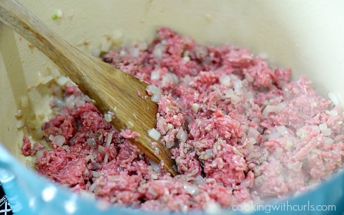 Ground beef stirred into the diced onion with a wood spatula.