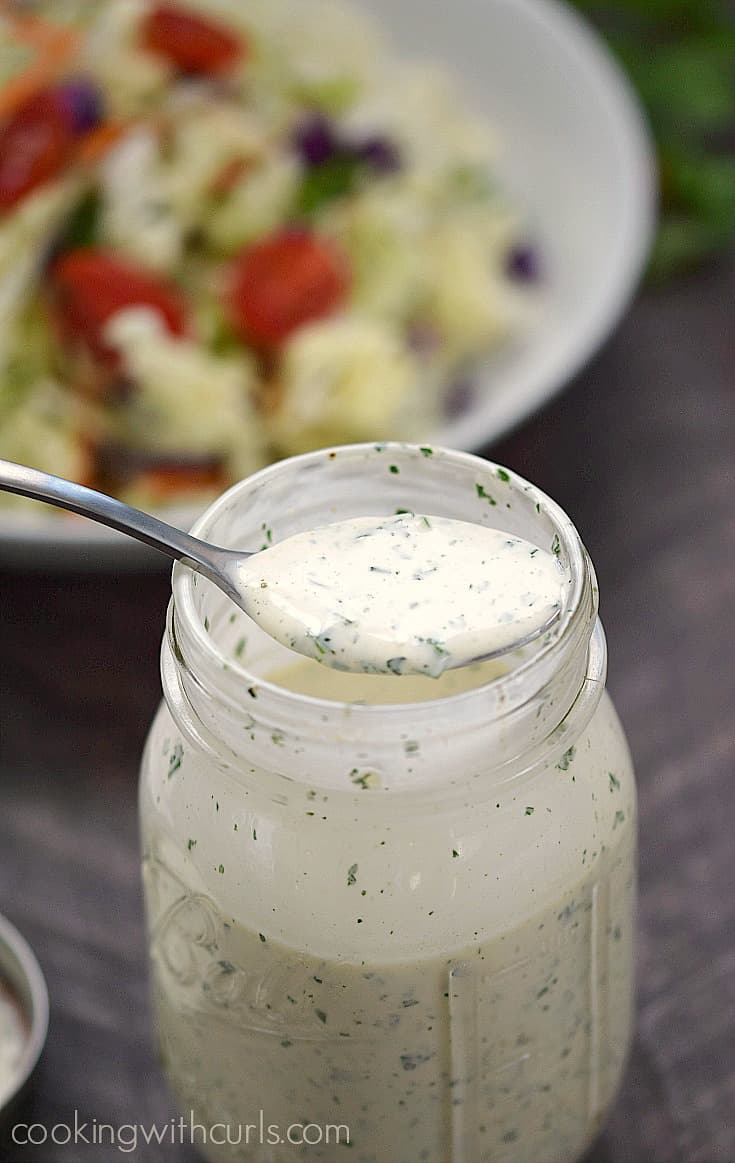 A spoon full of ranch dressing resting across the top of a jar full of dressing.