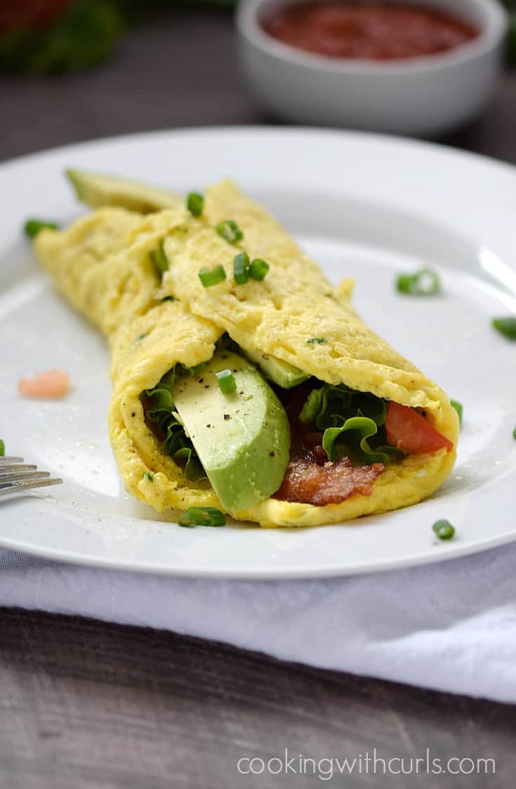 A thin scrambled egg "tortilla" wrapped around bacon, lettuce, tomato, and avocado slices on a small plate.