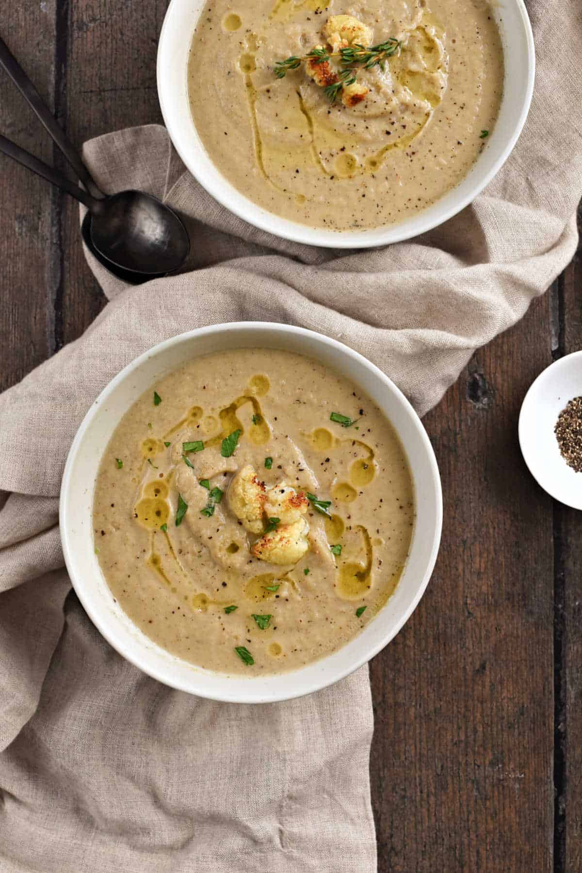 Two bowls of roasted cauliflower and garlic soup topped with roasted cauliflower pieces.