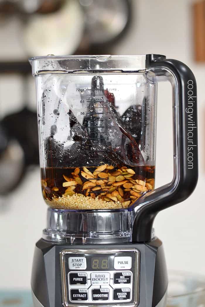 Raisin mixture added to a blender with cooking water and sesame seeds.