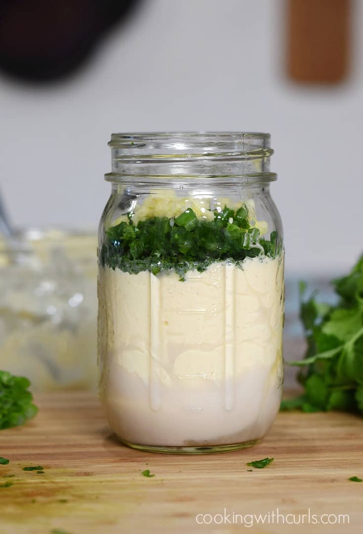 Milk, mayonnaise, green onions, and garlic layered in a glass jar.