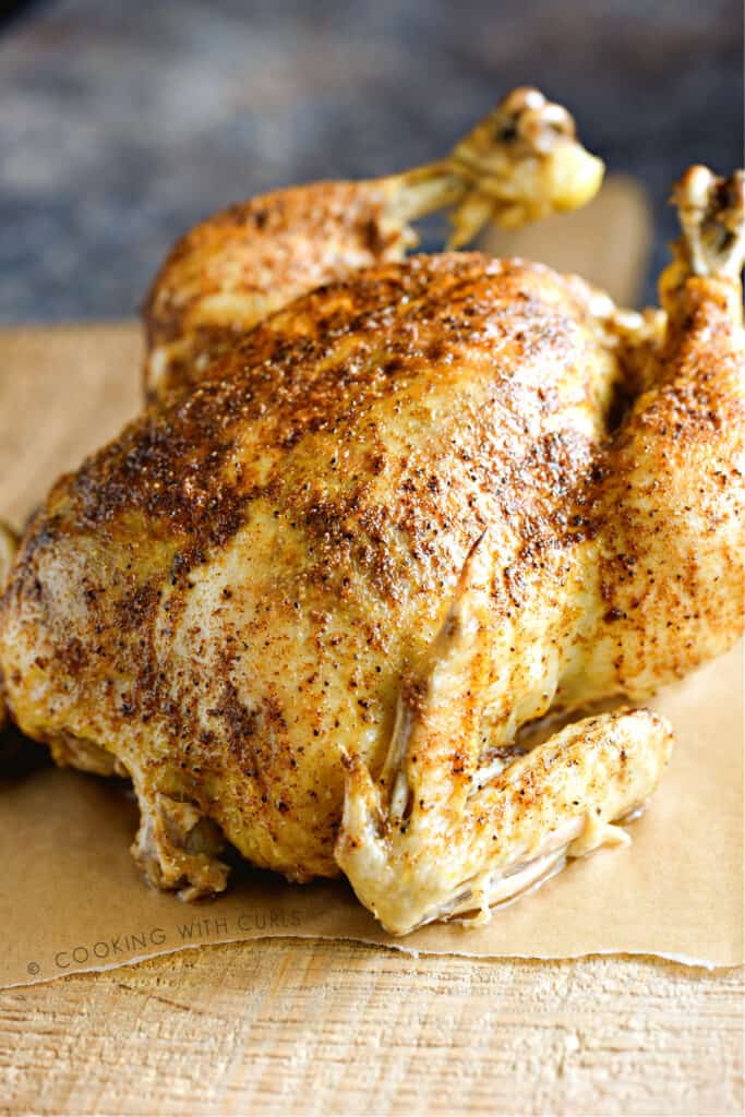 a close-up image of a cooked whole chicken on a wooden cutting board.