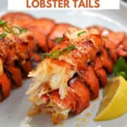 Two broiled lobster tails with garlic butter and lemon wedges on a plate with title graphic across the top.