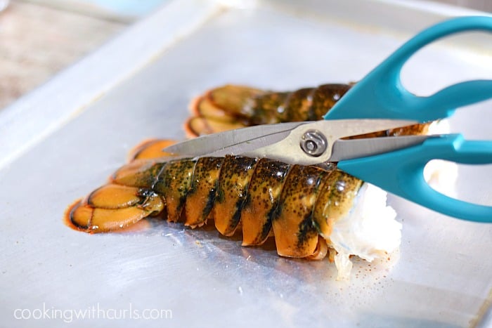 Kitchen sheers cutting through the center of the lobster tail shell.