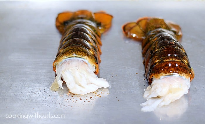 Two raw lobster tails, shell side up, on a baking sheet.
