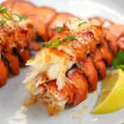 Two broiled lobster tails with lemon wedges on a plate.