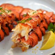 Two broiled lobster tails with garlic butter and lemon wedges on a plate.