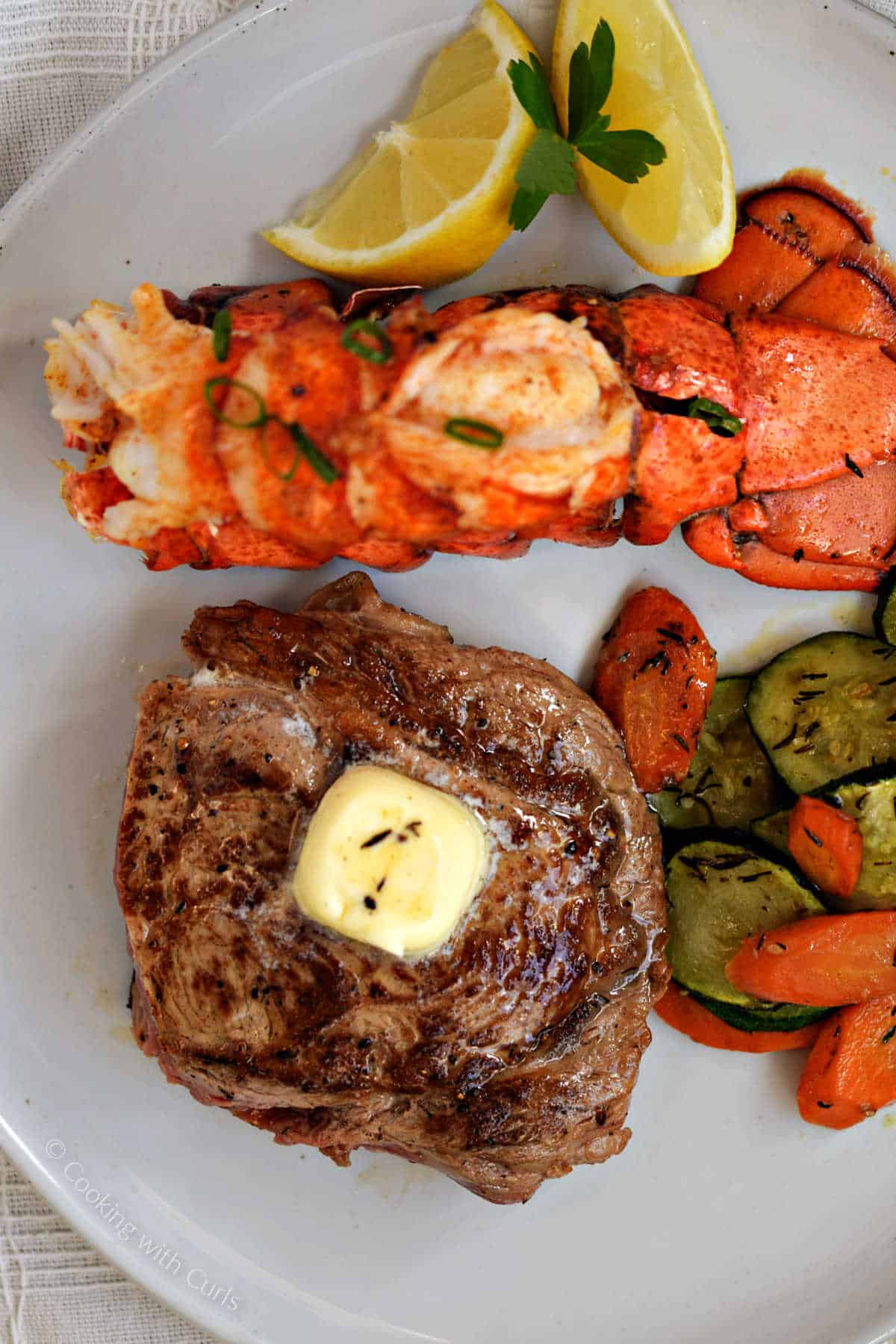 Broiled lobster tail and steak with sautéed zucchini and carrots on the side.