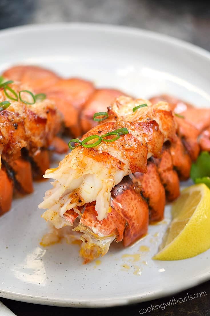 Two broiled lobster tails with lemon wedges on a plate.