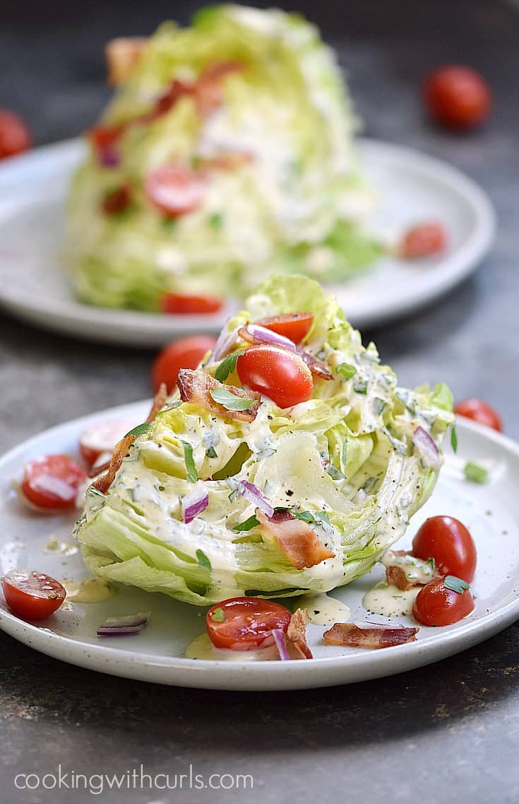 Two Wedge Salads topped with bacon, halved cherry tomatoes, and Homemade Ranch Dressing on two separate plates