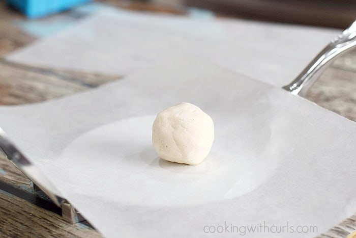 A cassava dough ball on a piece of parchment paper in a tortilla press.