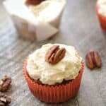 Paleo Maple Carrot Cupcakes in orange or white wrappers on a wooden board with pecans scattered around