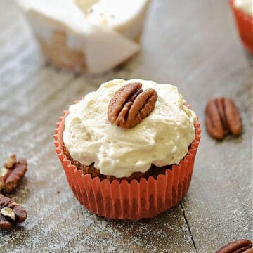 Paleo Maple Carrot Cupcakes in paper liners topped with maple frosting and pecan halves.