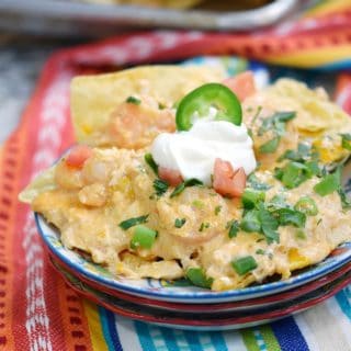 a plate loaded with creamy seafood nachos topped with sour cream and green onions sitting on a colorful napkin