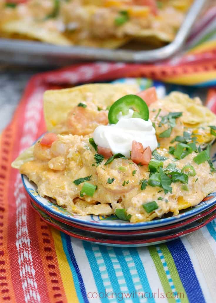 a plate loaded with creamy seafood nachos topped with sour cream and green onions sitting on a colorful napkin