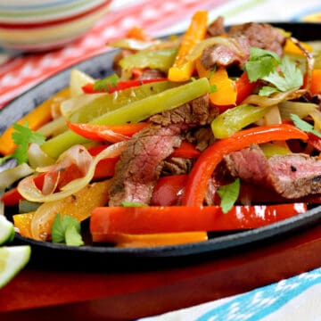 Strips of charred steak, bell peppers and onions in a fajita skillet.