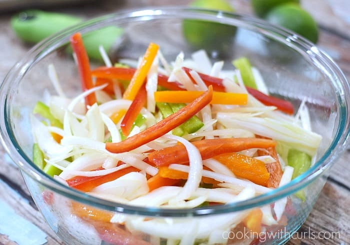 A glass bowl filled with thin strips of onion, red, yellow, and green bell peppers.