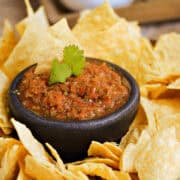 A small bowl of restaurant style blender salsa surrounded by tortilla chips.