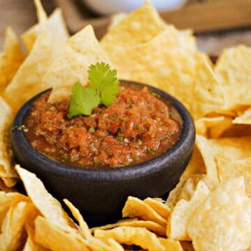A small bowl of restaurant style blender salsa surrounded by tortilla chips.