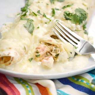Two seafood filled enchiladas on a plate covered in creamy sauce.