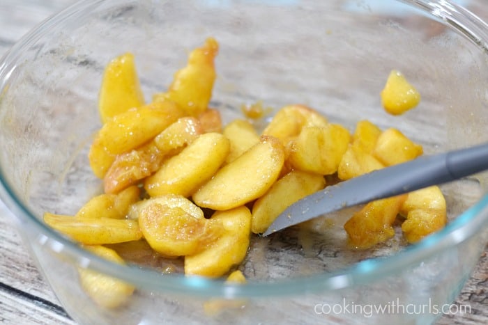 Fresh peach slices tossed with spices, sugar, cornstarch and vanilla in a large bowl.