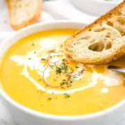A bowl of creamy carrot soup with crusty bread on the edge.