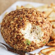 Cheese ball with chopped nuts on a plate with crackers.