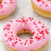 Vanilla donuts topped with pink icing and sprinkles.