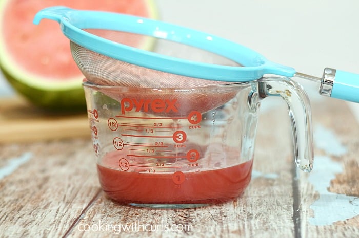 A strainer sitting on top of a large measuring cup straining out the watermelon pulp.