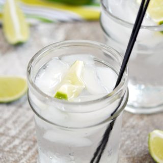 Two Classic Gin and Tonic in a clear glass garnished with a lime wedge and thin black cocktail straws.