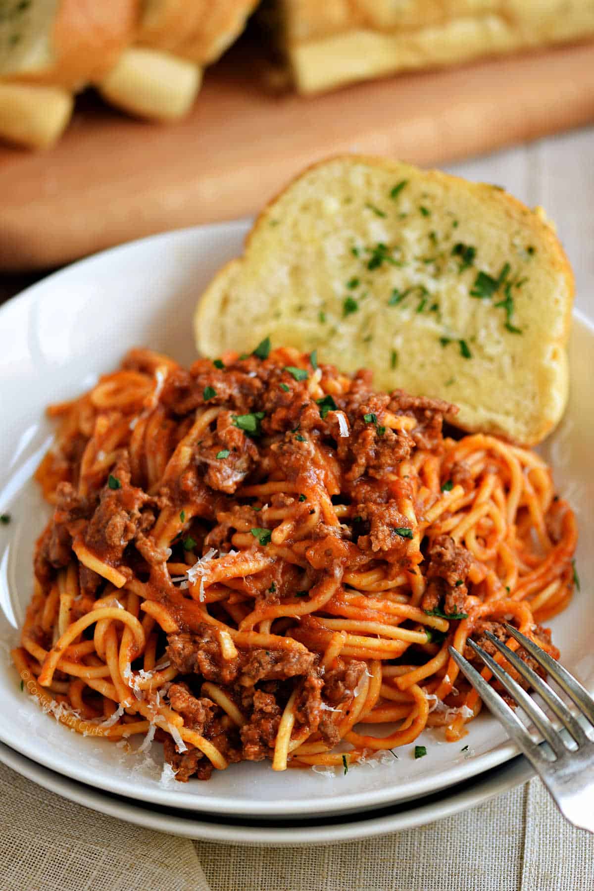 A bowl of spaghetti and meat sauce with a slice of garlic bread on the side.