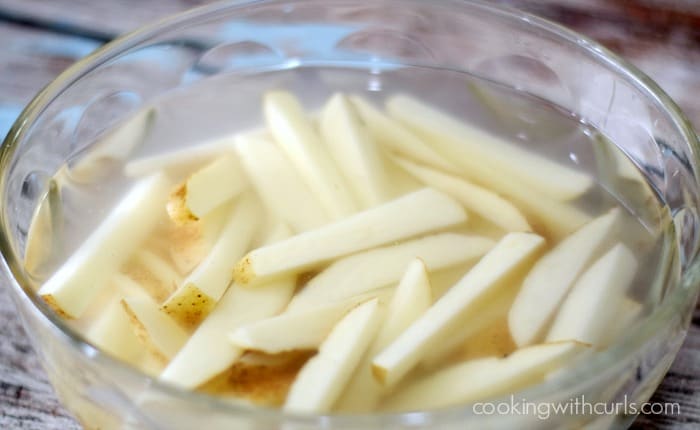 potato strips in water, in a glass bowl.
