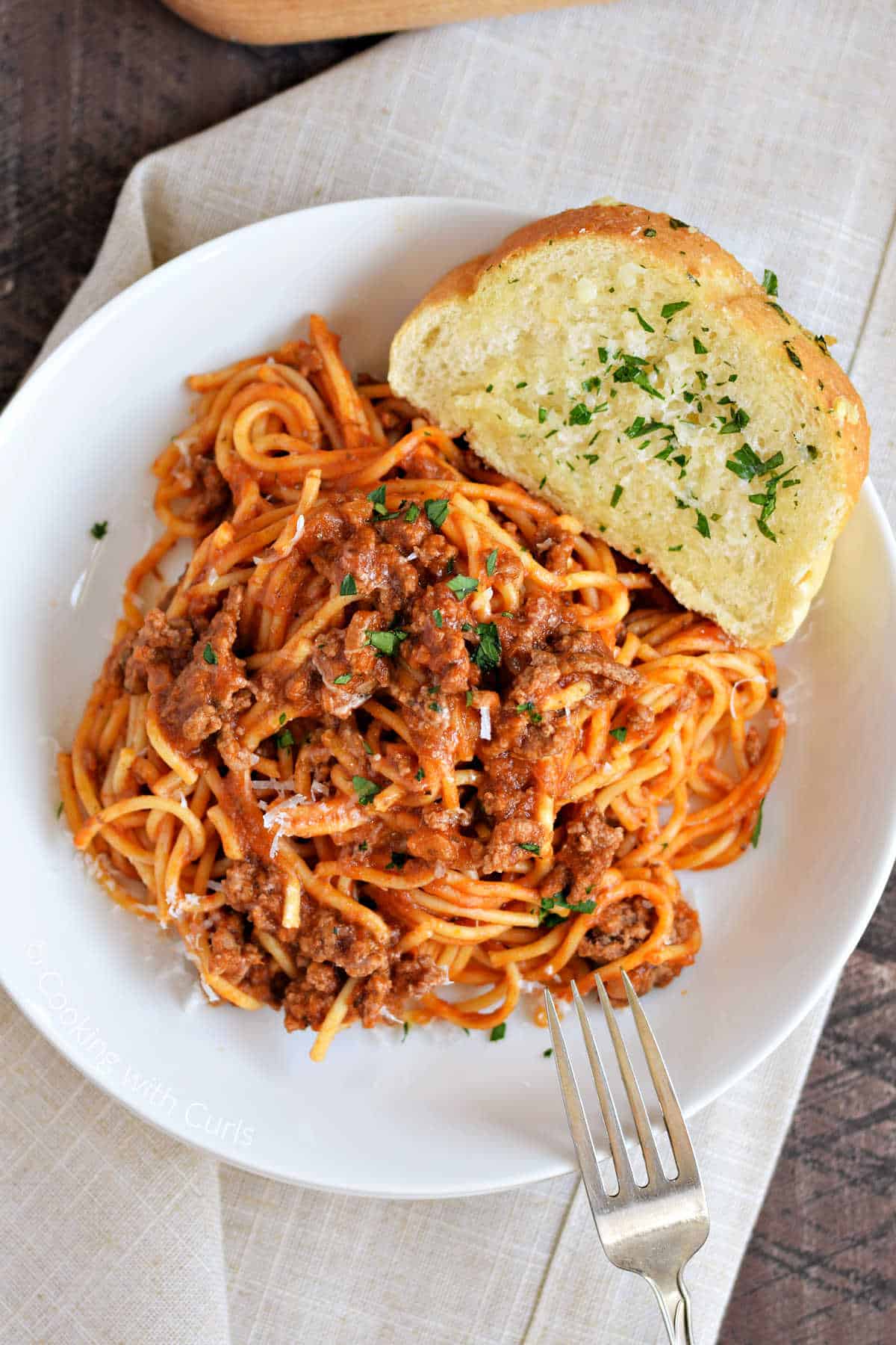 A bowl of spaghetti with a slice of garlic bread on the rim of the bowl.