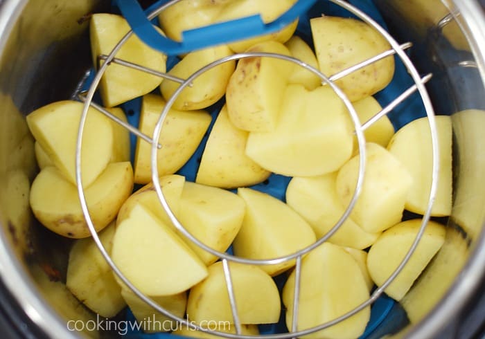 Potato chunks in a blue silicone steamer basket topped with a metal trivet.