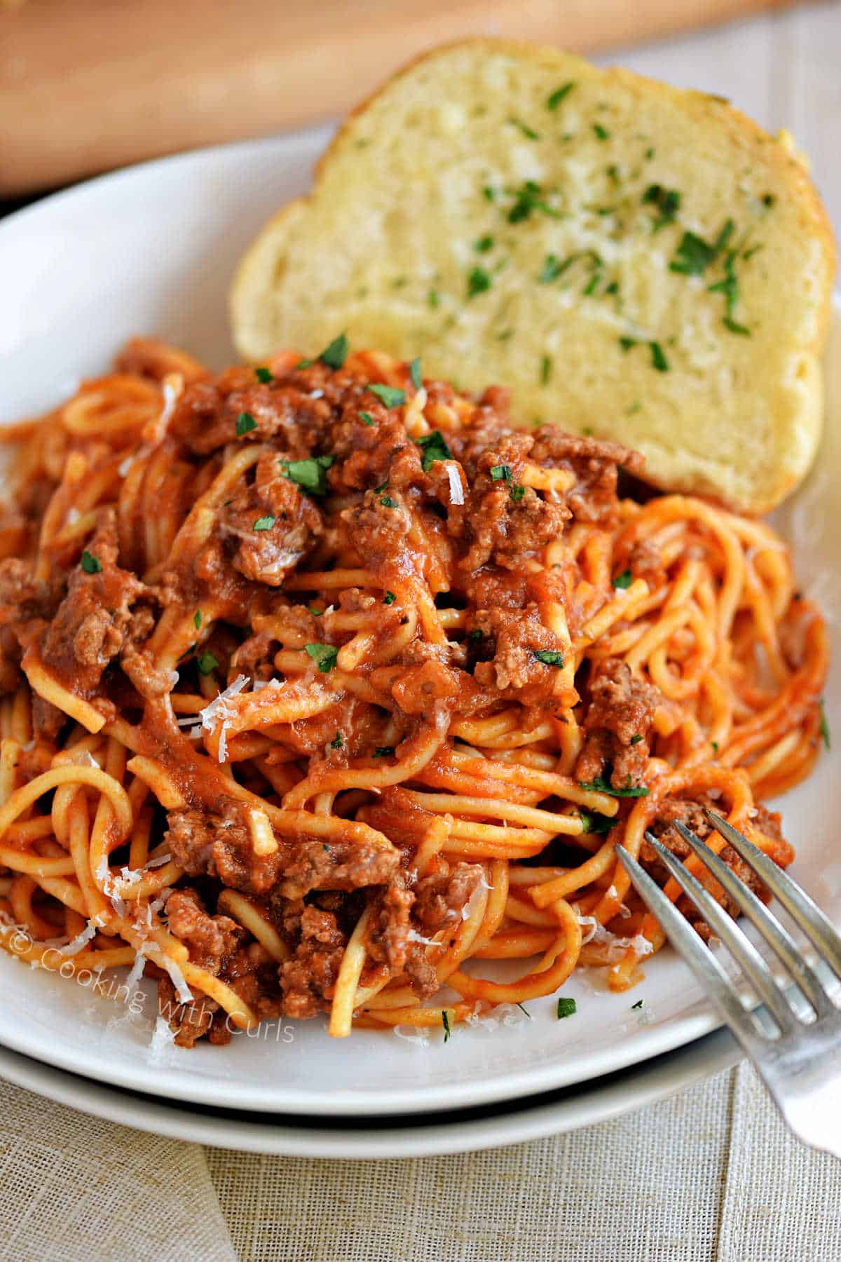 Spaghetti with meat sauce on a white plate with garlic bread on the side.