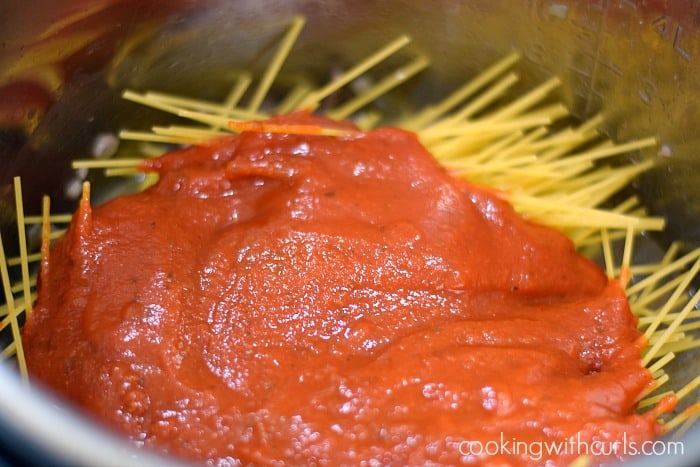 Spaghetti sauce poured over uncooked spaghetti noodles.