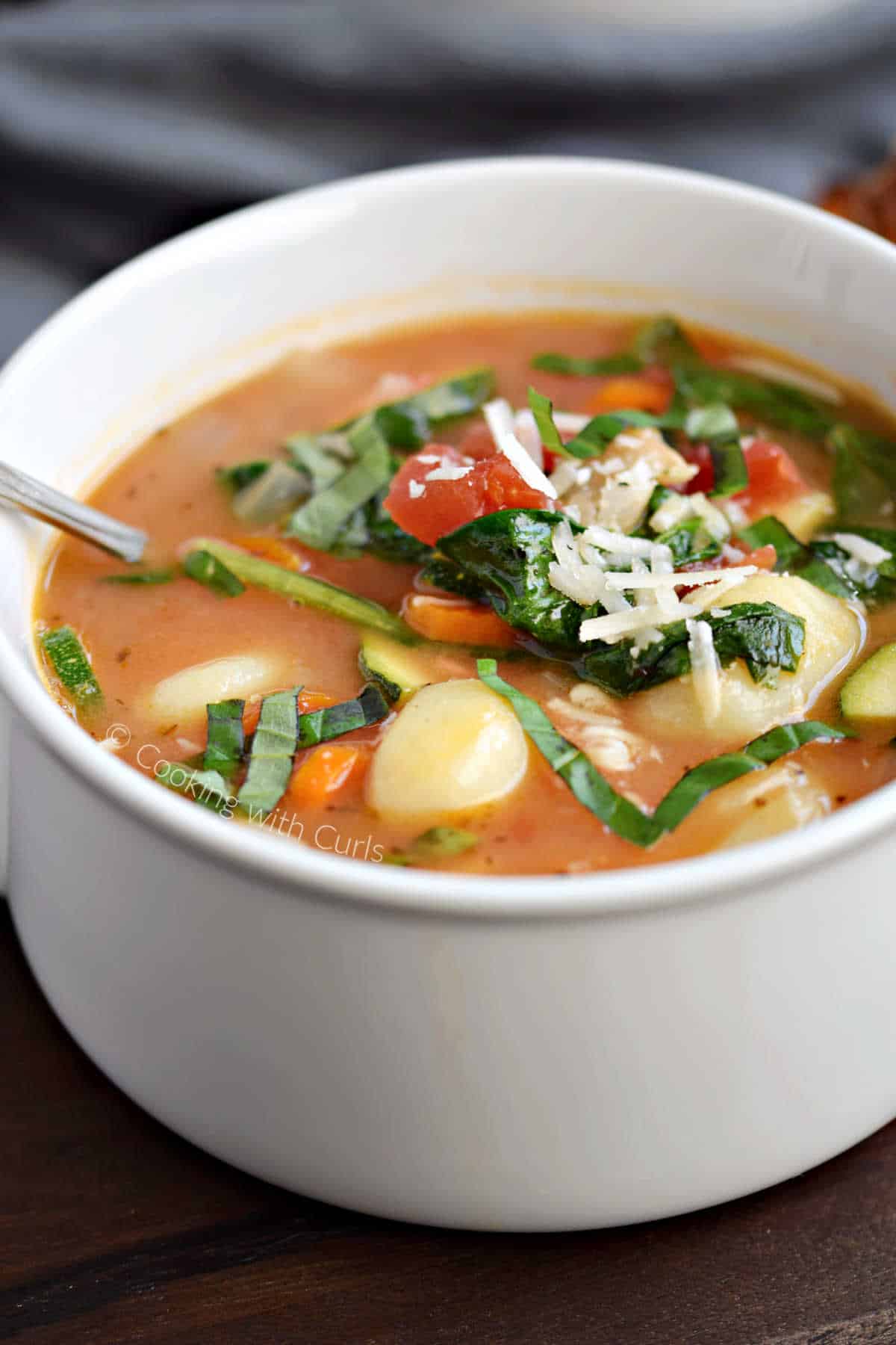 Gnocchi, carrots, zucchini, tomatoes, spinach, and grated parmesan in a soup bowl.