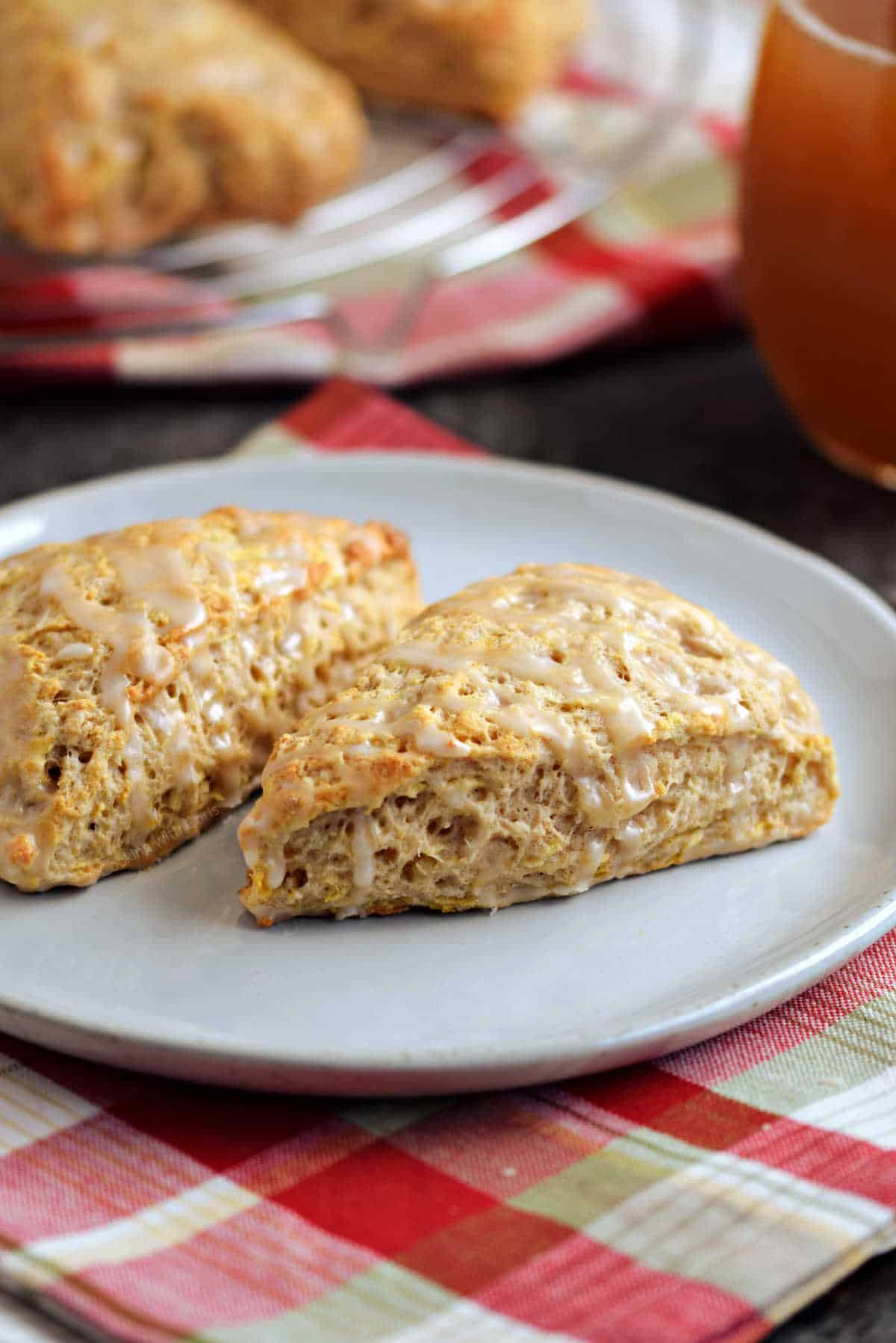 Two apple scones on a plate with a glass of apple cider in the background.