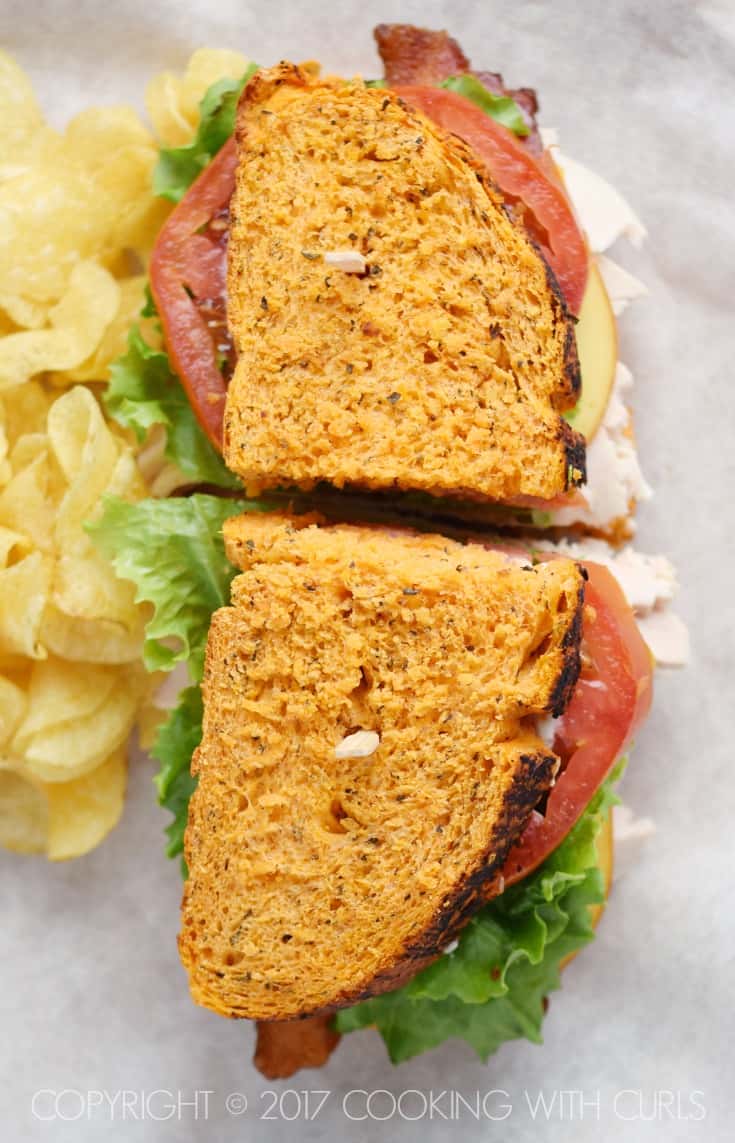 Looking down on tomato sandwich bread with tomato, lettuce and turkey with potato chips on the side.