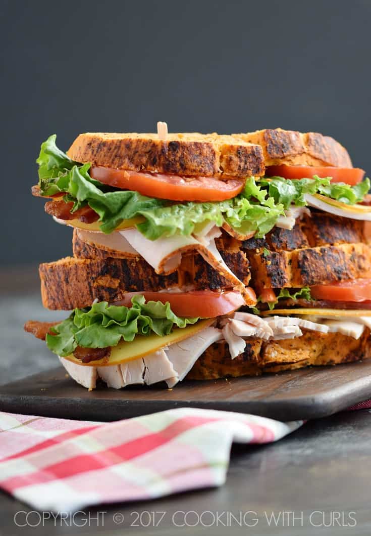 Two turkey, cheese, lettuce, and tomato sandwiches with tomato bread sliced in half and stacked on top of each other.