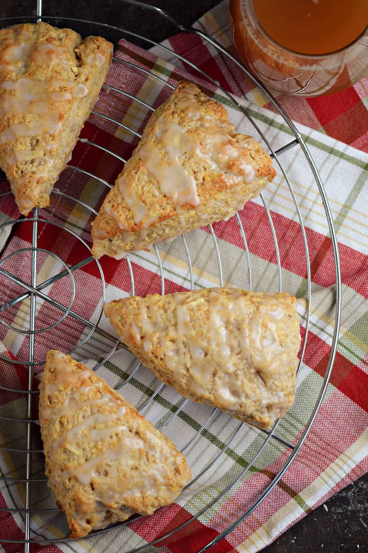 Four apple scones with glaze on wire rack.