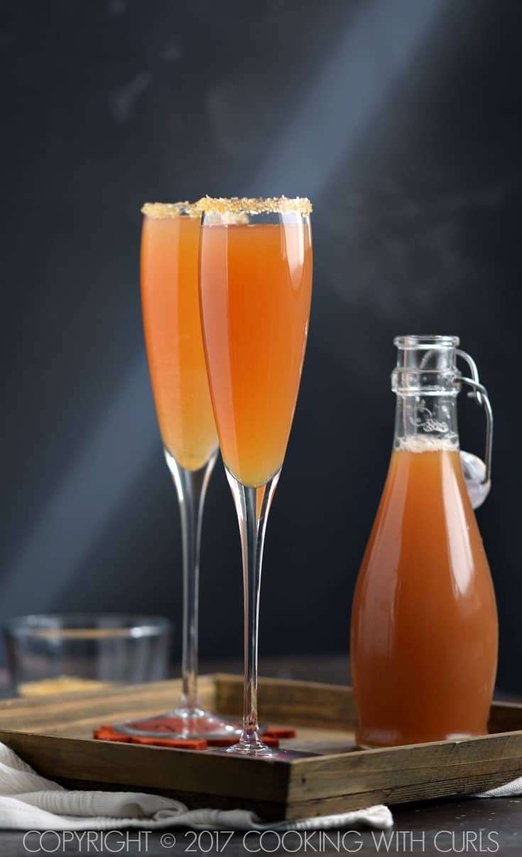 Two champagne flutes filled with apple cider, cognac and Prosecco with gold sugar around the rim.