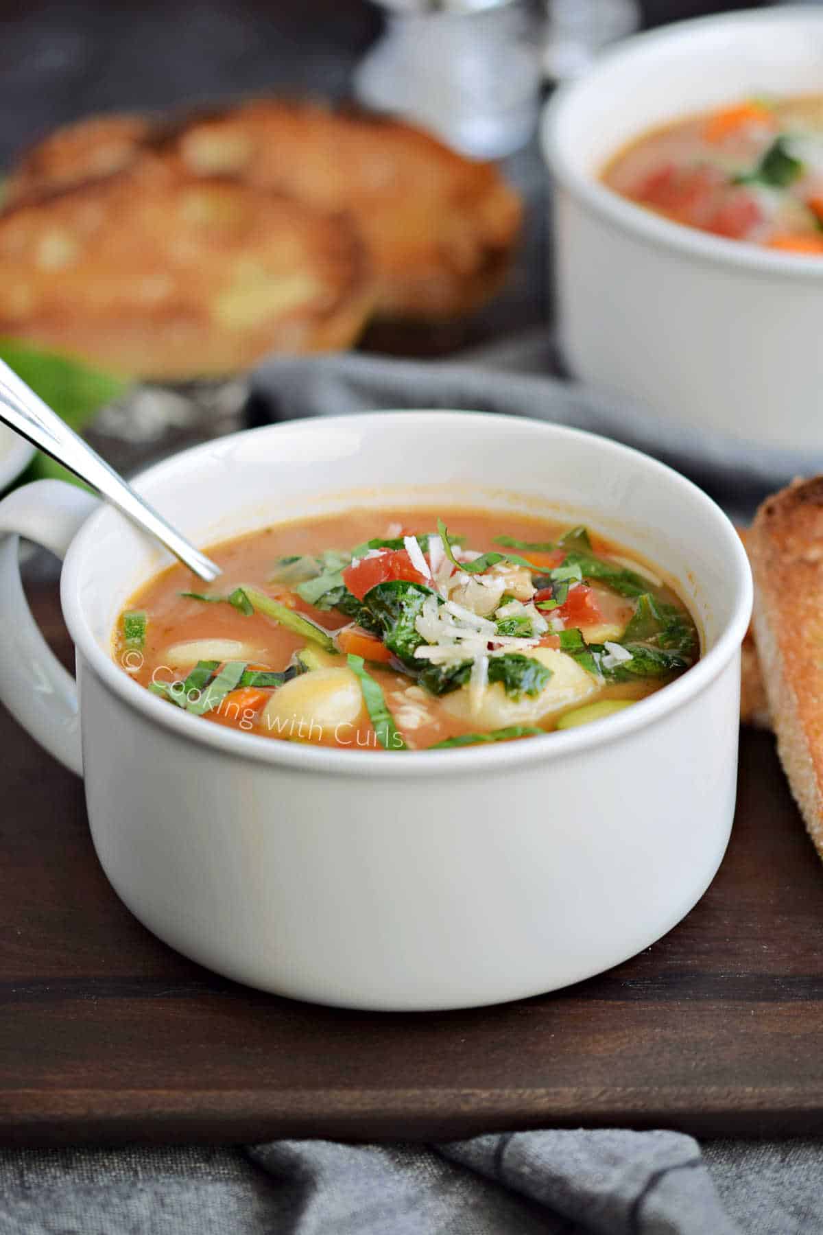 Parmesan Gnocchi Soup in a bowl sitting on a wooden board with toasted bread.