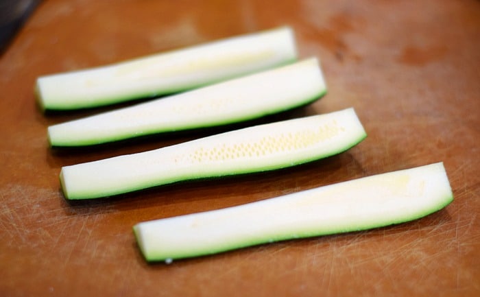 Zucchini cut into four quarters on a cutting board.