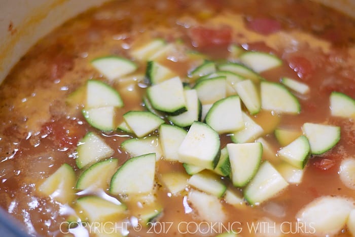 Sliced zucchini and gnocchi added to simmering soup in a large pot.