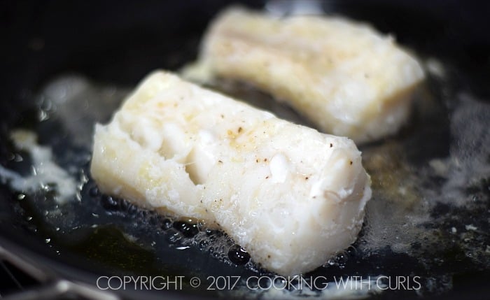 Two cod filets cooking in a skillet.