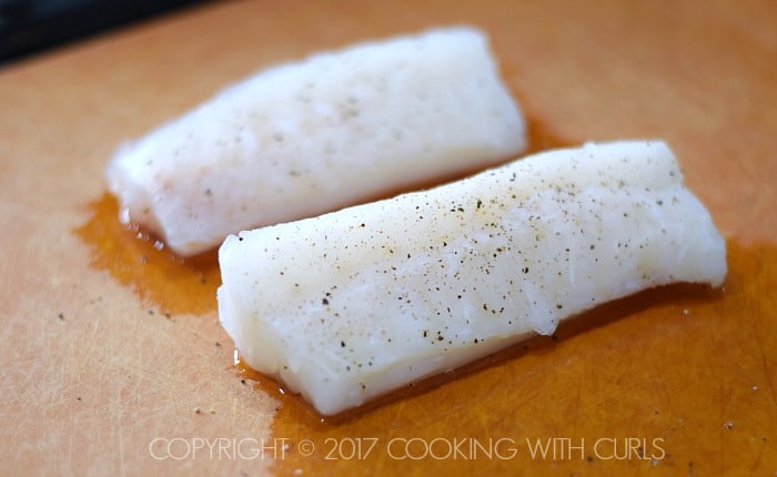 Two seasoned cod fillets on a cutting board.