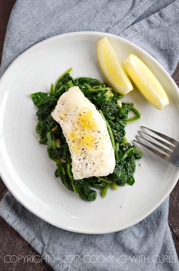 Looking down on a cod filet on a bed of cooked spinach garnished with pepper and lemon zest.